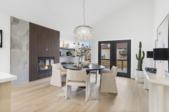 dining room featuring french doors, a tiled fireplace, a chandelier, and light wood-type flooring