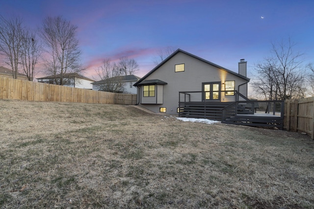 back house at dusk with a wooden deck and a lawn