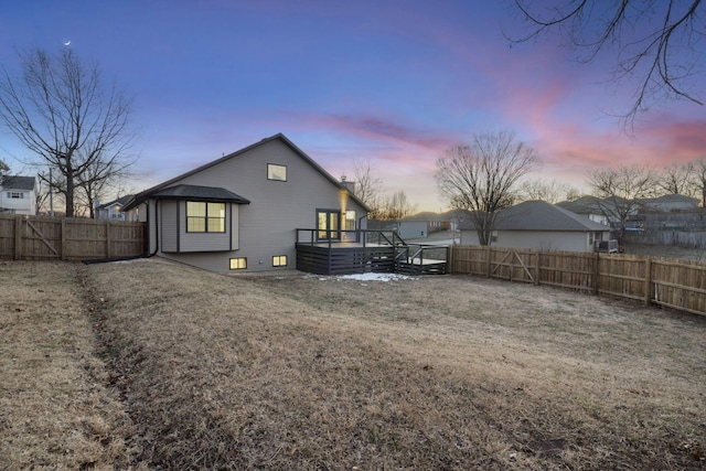 back house at dusk featuring a lawn and a deck