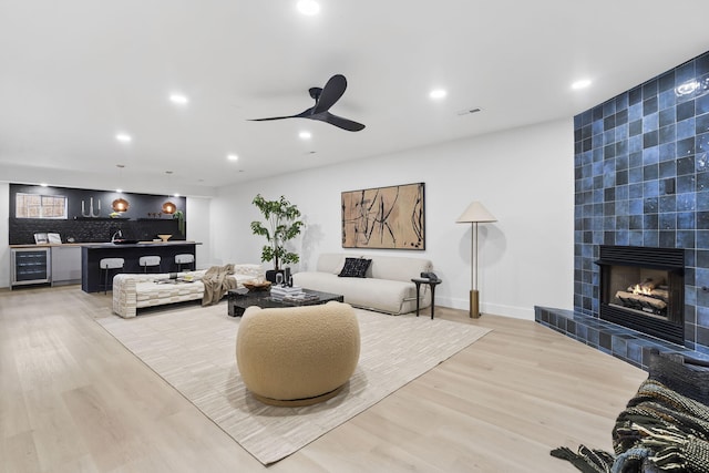 living room with wine cooler, a fireplace, light wood-type flooring, and bar area