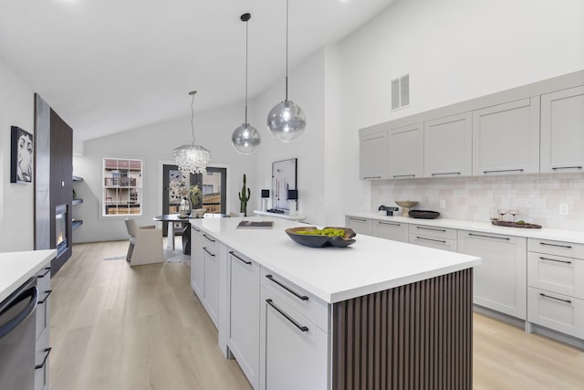 kitchen featuring dishwasher, backsplash, hanging light fixtures, a kitchen island with sink, and light hardwood / wood-style floors