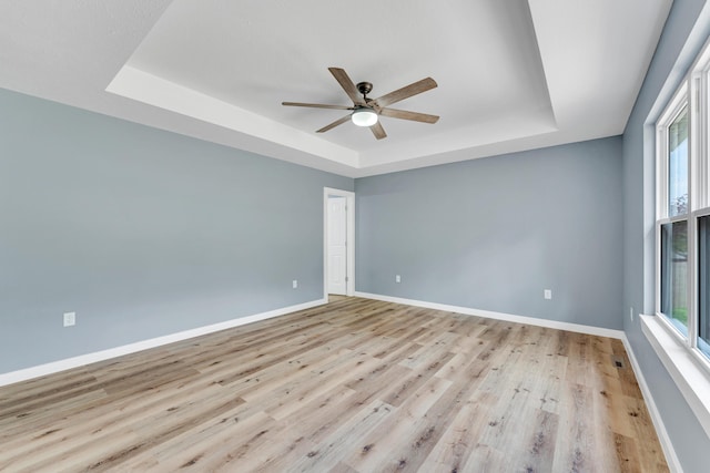 spare room with a tray ceiling, light hardwood / wood-style flooring, and ceiling fan