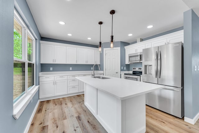 kitchen featuring appliances with stainless steel finishes, decorative light fixtures, sink, white cabinets, and a kitchen island with sink