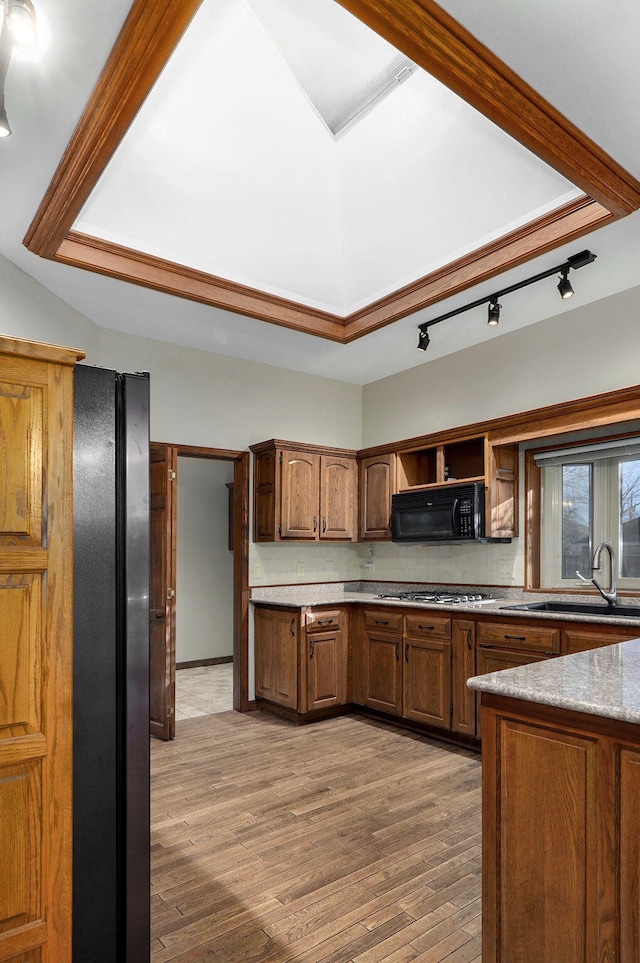 kitchen with sink, tasteful backsplash, stainless steel gas stovetop, light stone countertops, and light hardwood / wood-style floors