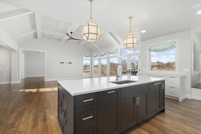 kitchen with pendant lighting, sink, dark wood-type flooring, a kitchen island with sink, and vaulted ceiling with beams