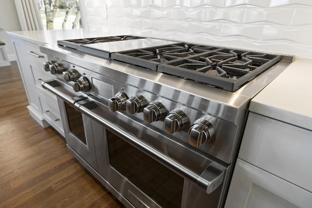 room details with tasteful backsplash, dark hardwood / wood-style floors, white cabinets, and range with two ovens