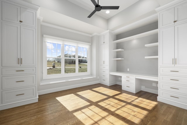 unfurnished office with dark wood-type flooring, built in desk, ornamental molding, and ceiling fan