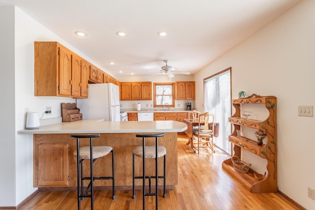 kitchen featuring white appliances, ceiling fan, a kitchen breakfast bar, kitchen peninsula, and light wood-type flooring