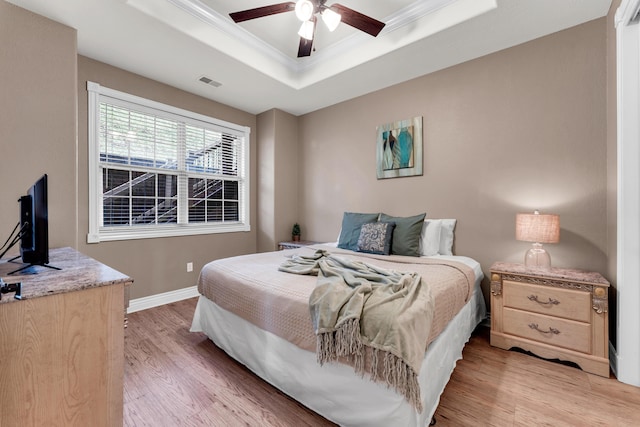 bedroom featuring crown molding, a tray ceiling, light hardwood / wood-style flooring, and ceiling fan