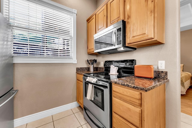 kitchen featuring stainless steel appliances, light tile patterned flooring, dark stone countertops, and light brown cabinets