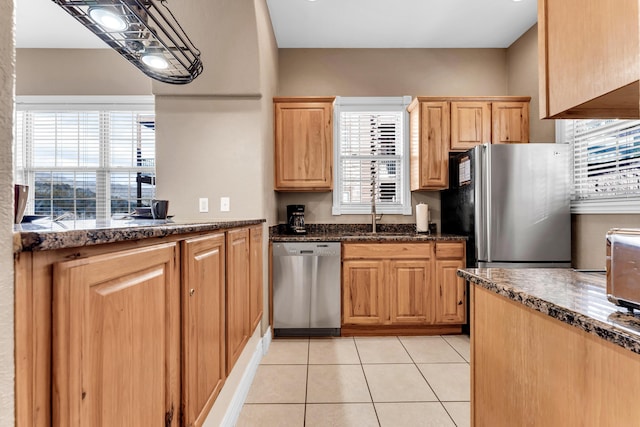 kitchen with appliances with stainless steel finishes, sink, dark stone counters, and light tile patterned floors