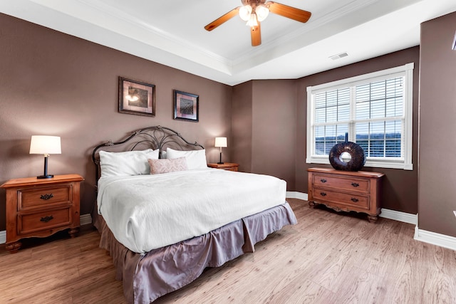 bedroom featuring crown molding, ceiling fan, a tray ceiling, and light hardwood / wood-style flooring