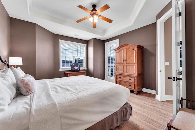 bedroom with crown molding, light wood-type flooring, ceiling fan, and a tray ceiling