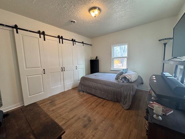 bedroom with dark hardwood / wood-style floors, a closet, a barn door, and a textured ceiling