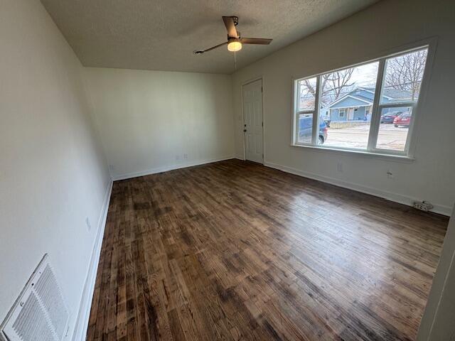 unfurnished room with a healthy amount of sunlight, dark wood-type flooring, ceiling fan, and a textured ceiling