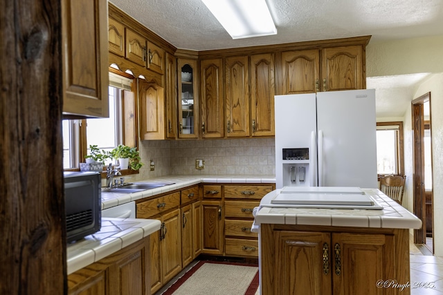 kitchen featuring a kitchen island, white fridge with ice dispenser, tile counters, and sink