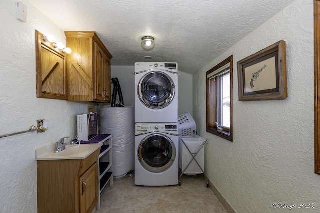 clothes washing area with stacked washer and clothes dryer, sink, cabinets, a textured ceiling, and light tile patterned floors