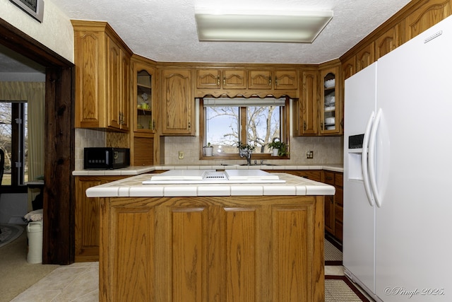 kitchen with a kitchen island, white refrigerator with ice dispenser, sink, and tile counters