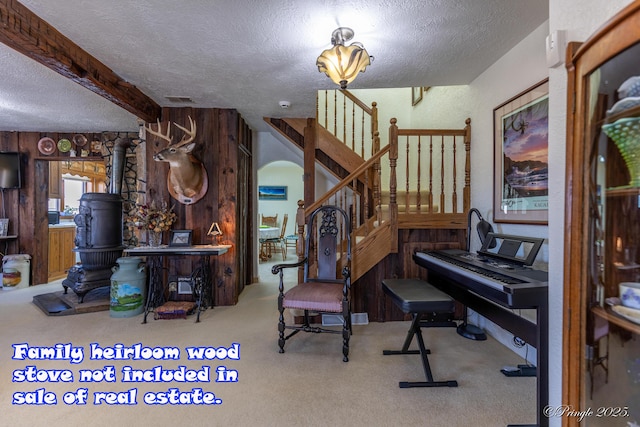 misc room featuring wood walls, a textured ceiling, a wood stove, beamed ceiling, and light colored carpet