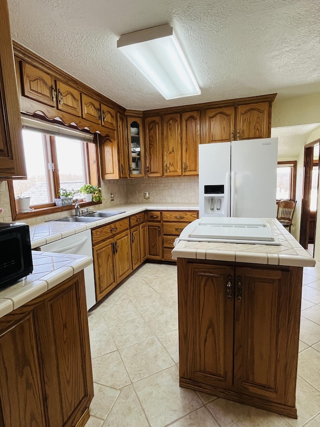 kitchen featuring sink, tile countertops, white fridge with ice dispenser, and a kitchen island