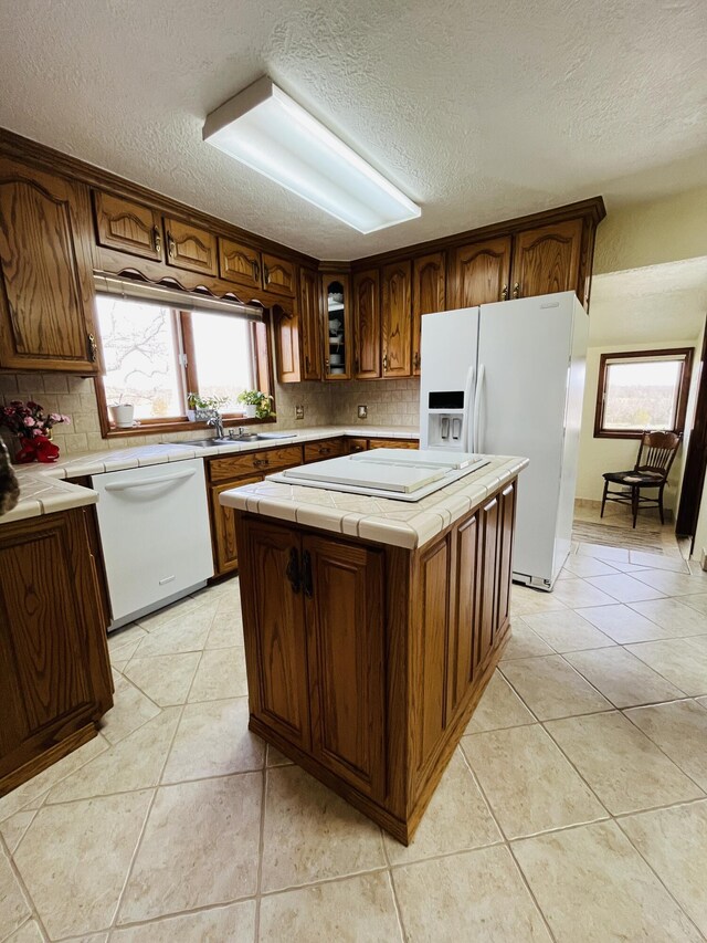 kitchen featuring light tile patterned flooring, white appliances, tile counters, and a center island