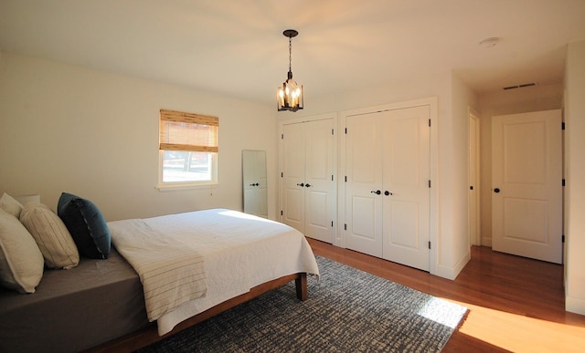 bedroom featuring wood-type flooring, two closets, and an inviting chandelier