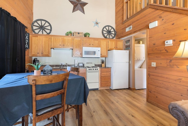 kitchen with a high ceiling, stacked washer and clothes dryer, white appliances, and light hardwood / wood-style flooring