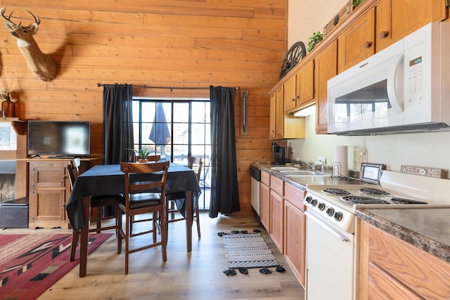 kitchen featuring sink, white appliances, light wood-type flooring, and wood walls