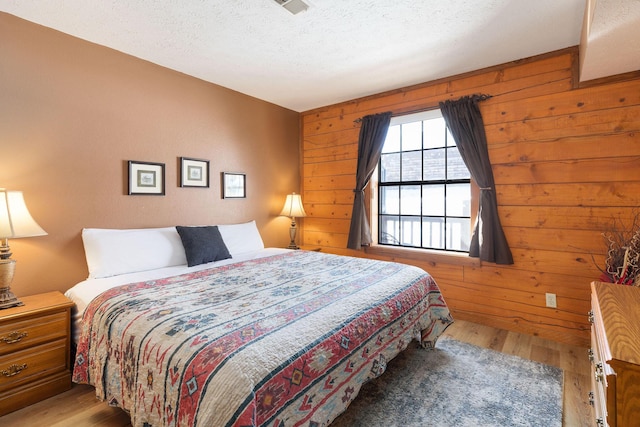 bedroom with wood-type flooring, wooden walls, and a textured ceiling