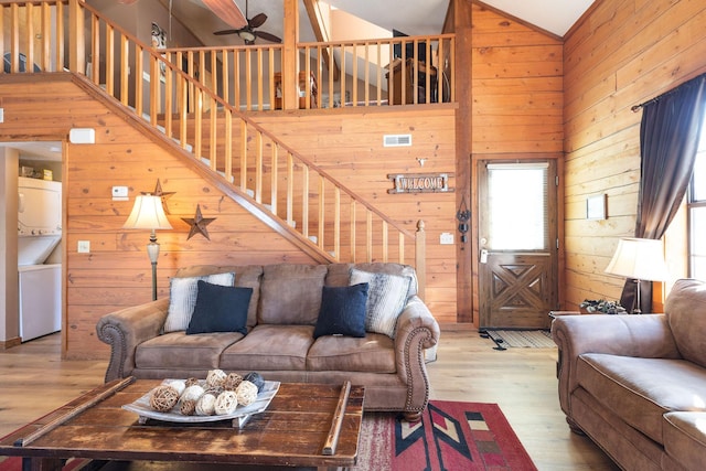 living room with ceiling fan, high vaulted ceiling, stacked washer / drying machine, and light hardwood / wood-style floors