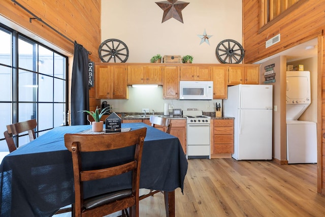 kitchen featuring stacked washer / drying machine, white appliances, sink, and a towering ceiling