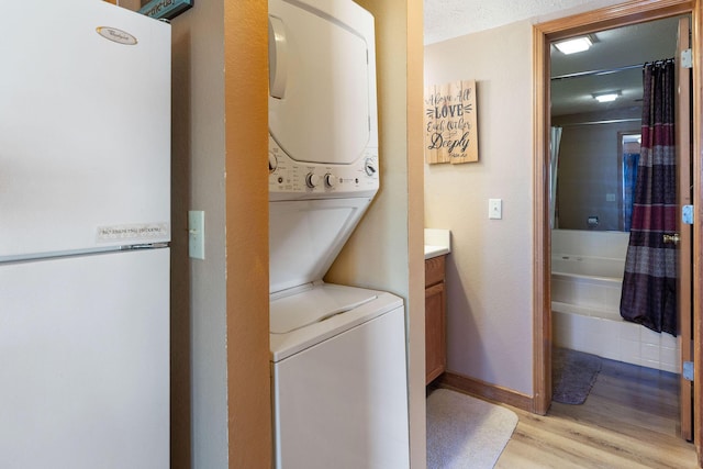 clothes washing area with stacked washer / dryer, light hardwood / wood-style floors, and a textured ceiling