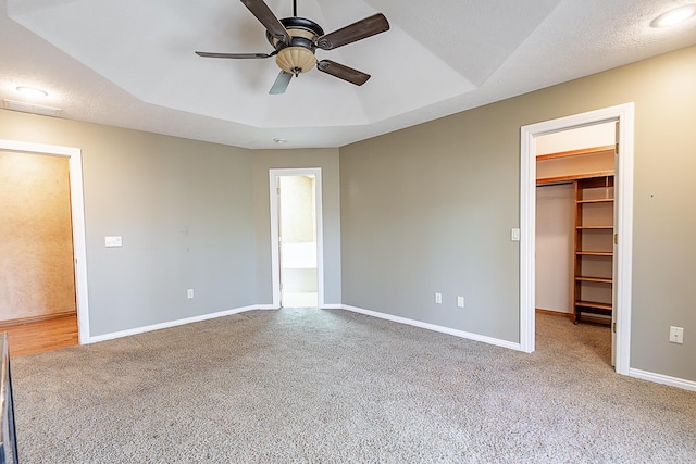 unfurnished bedroom featuring ceiling fan, carpet floors, a raised ceiling, a walk in closet, and a closet