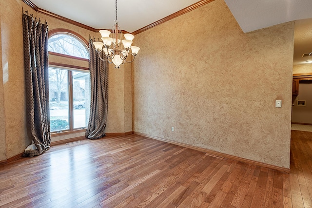 empty room featuring hardwood / wood-style flooring, ornamental molding, and an inviting chandelier