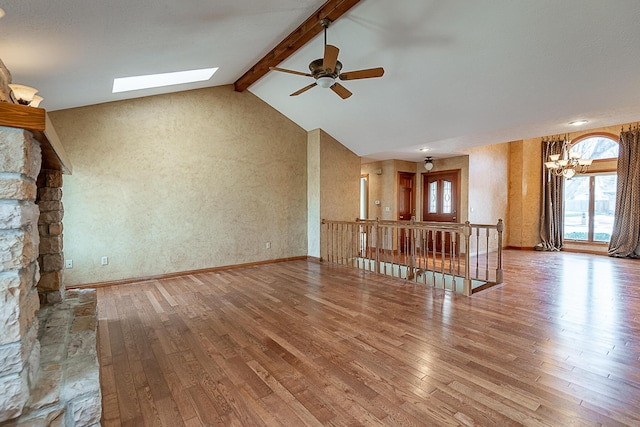 unfurnished living room with wood-type flooring, vaulted ceiling with skylight, and ceiling fan with notable chandelier