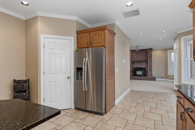 kitchen with ornamental molding, stainless steel fridge with ice dispenser, a brick fireplace, and dark stone counters