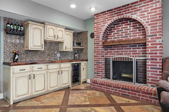 kitchen with sink, backsplash, wine cooler, a brick fireplace, and cream cabinetry