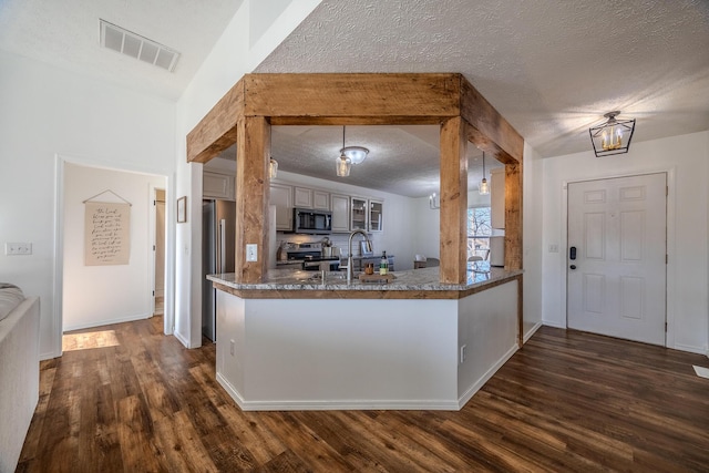 kitchen featuring sink, appliances with stainless steel finishes, a textured ceiling, dark hardwood / wood-style flooring, and kitchen peninsula