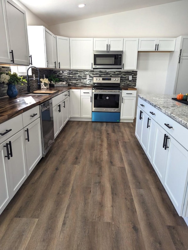 kitchen with vaulted ceiling, appliances with stainless steel finishes, butcher block countertops, white cabinets, and decorative backsplash