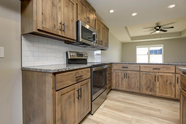 kitchen with appliances with stainless steel finishes, kitchen peninsula, decorative backsplash, and dark stone counters