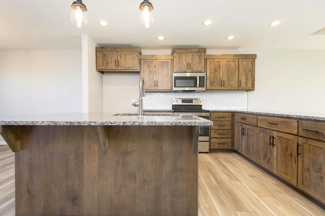 kitchen featuring sink, light hardwood / wood-style flooring, appliances with stainless steel finishes, light stone counters, and tasteful backsplash