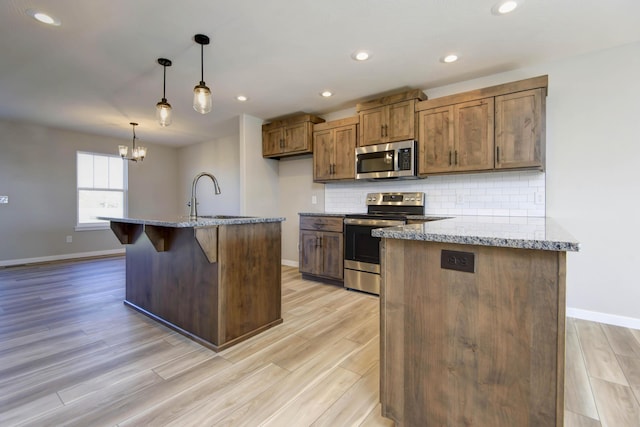 kitchen featuring sink, light stone counters, decorative light fixtures, an island with sink, and stainless steel appliances