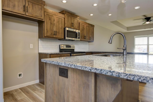 kitchen with sink, decorative backsplash, light stone counters, stainless steel appliances, and light wood-type flooring