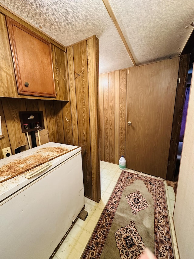 laundry area featuring a textured ceiling and wood walls