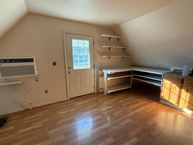 interior space featuring wood-type flooring, vaulted ceiling, and a wall mounted air conditioner