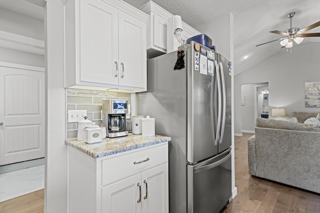 kitchen featuring stainless steel refrigerator, white cabinets, ceiling fan, light stone countertops, and backsplash