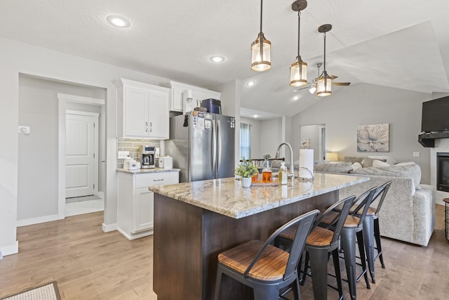 kitchen featuring stainless steel refrigerator, hanging light fixtures, tasteful backsplash, an island with sink, and white cabinets