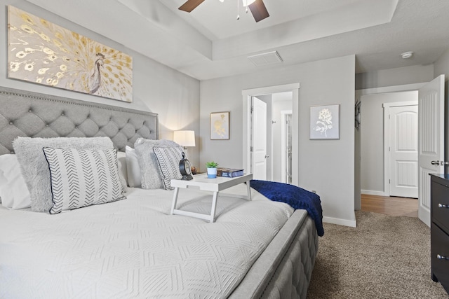 carpeted bedroom with ceiling fan and a tray ceiling