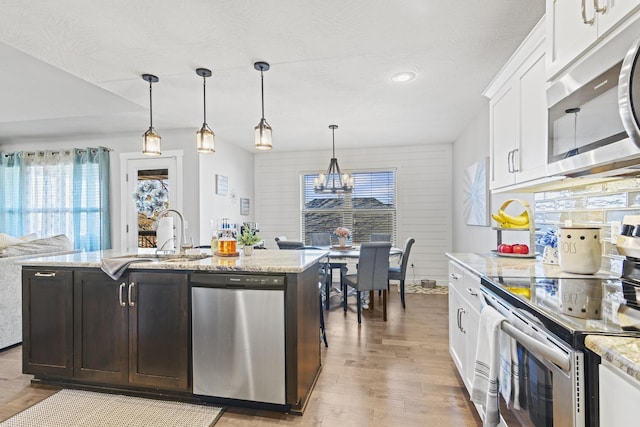 kitchen with sink, appliances with stainless steel finishes, an island with sink, pendant lighting, and white cabinets