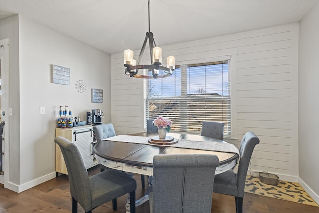 dining area featuring dark wood-type flooring, wood walls, and a notable chandelier